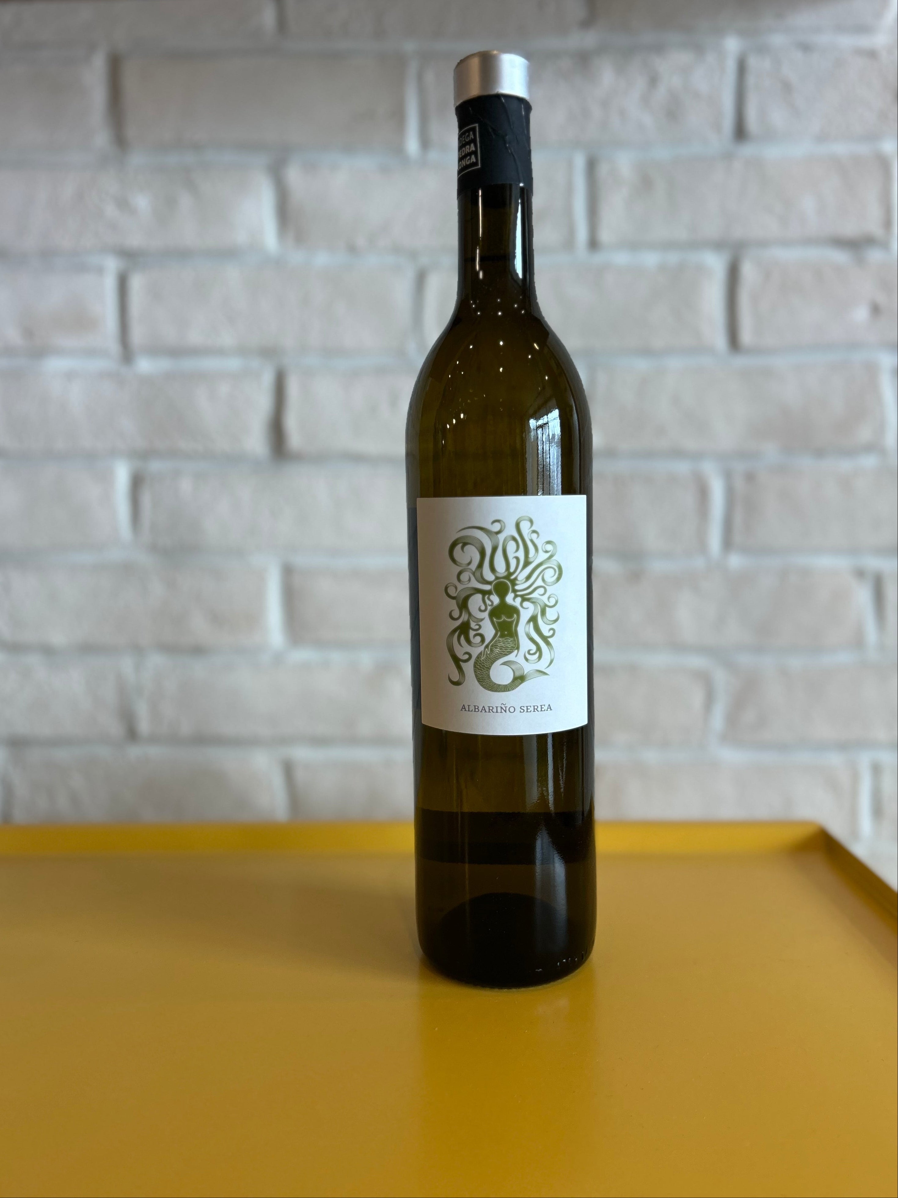 Wine bottle with a decorative label on a yellow surface with a light gray brick wall background
