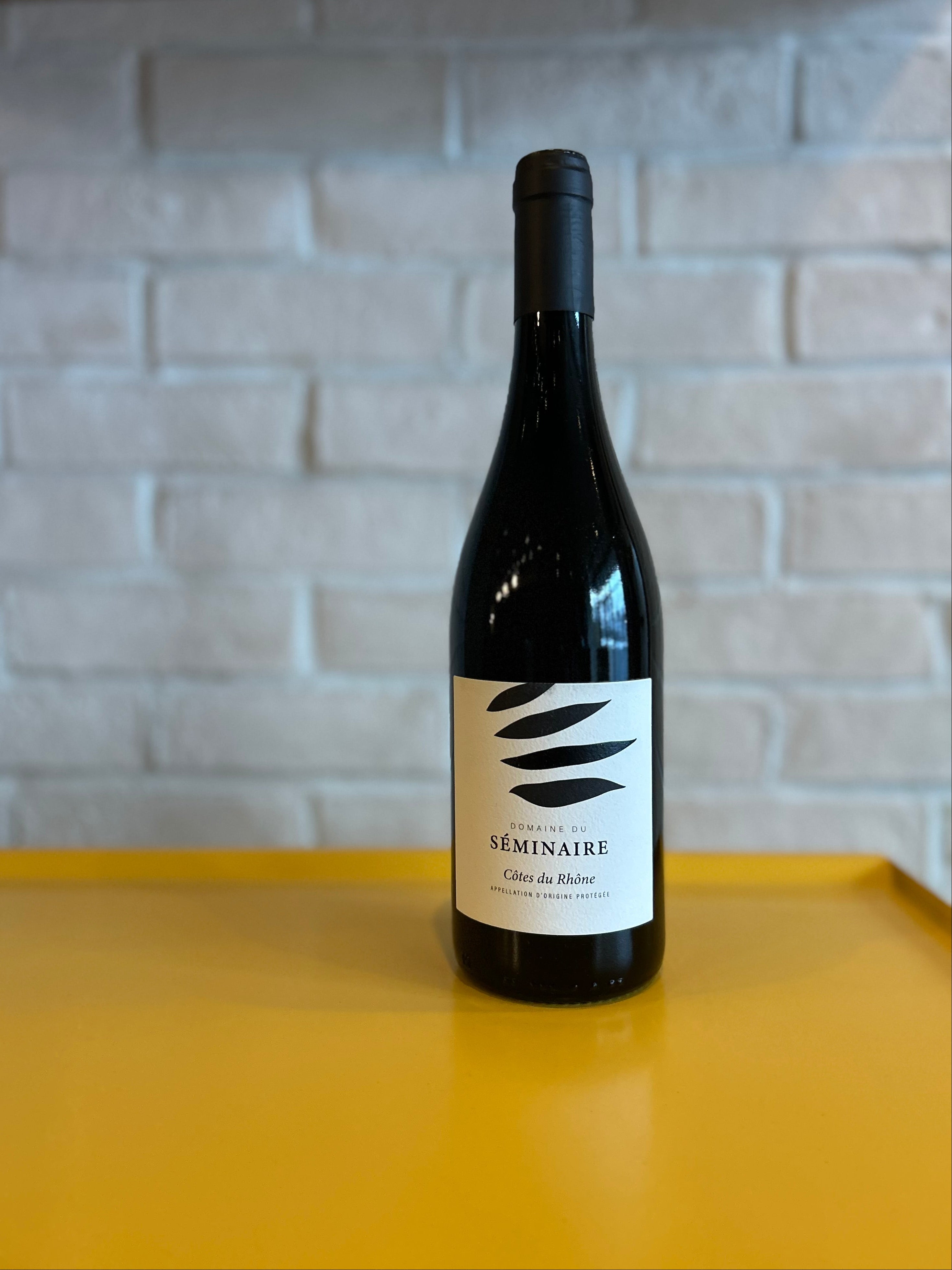 Wine bottle with a label on a yellow surface and light gray brick wall background